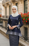 Woman wearing a Kurung Kedah Blue Black Silver traditional outfit with a white instant shawl hijab in an urban setting.