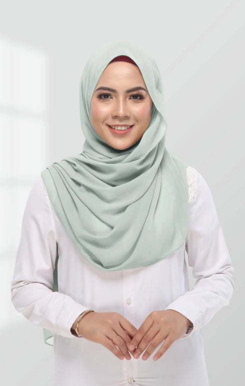 Studio portrait of a smiling woman wearing a dusty green semi-instant chiffon shawl styled neatly over a white blouse, soft natural makeup, clean light grey background, elegant and minimal fashion shoot