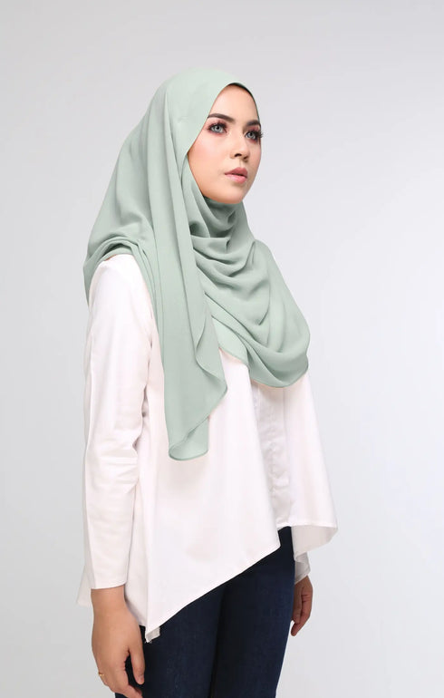 Woman wearing a Dusty Green flat lay showing overall size and plain design hijab, plain white shirt, and dark pants on a plain background