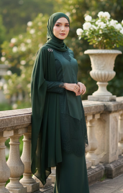 Woman in a Kebaya Moden Emerald Green side view on model highlighting long sleeve fit dress and Emerald Green Shawl hijab standing outdoors with decorative elements.