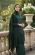 Woman in a Kebaya Moden Emerald Green side view on model highlighting long sleeve fit dress and Emerald Green Shawl hijab standing outdoors with decorative elements.