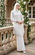 Woman in a Pearl White outfit Kebaya Moden side view on model highlighting long straight sleeves on a stone balcony with floral decorations.