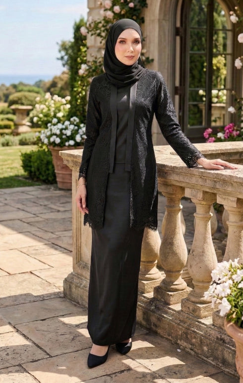 Woman styling kebaya Kutu Baru Black front view with comfortable fit and long sleeve design standing outdoors near decorative stone railing with flowers and greenery.