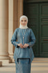 Woman wearing a C Luxe Kurung Kedah Teal Blue patterned outfit with a hijab, standing against a plain background