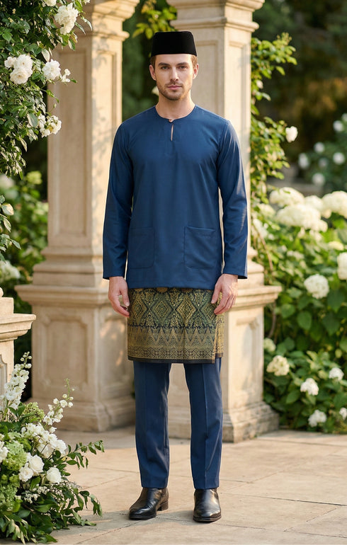 Man wearing a Baju Melayu Teluk Belanga Dark Teal Blue traditional outfit with a sampin Exclusive 3d skirt, standing in a decorative garden.