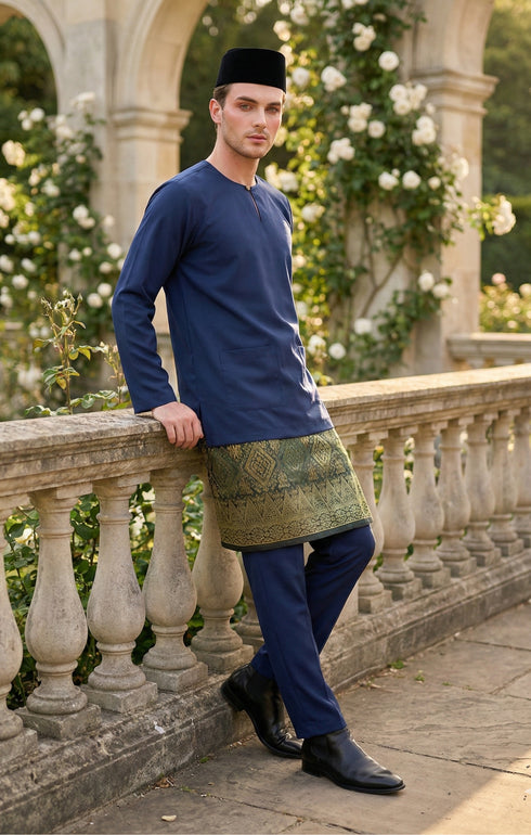 Man in traditional attire Baju Melayu Teluk Belanga Navy Blue standing on a stone balcony with floral decorations.