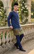 Man in traditional attire Baju Melayu Teluk Belanga Navy Blue standing on a stone balcony with floral decorations.