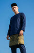 Man wearing a Baju Melayu Teluk Belanga Navy Blue outfit with a Sampin 3D Exclusive against a clear blue sky