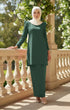 Woman in a Kurung moden plain dark emerlad green full outfit view standing on a balcony with floral decorations