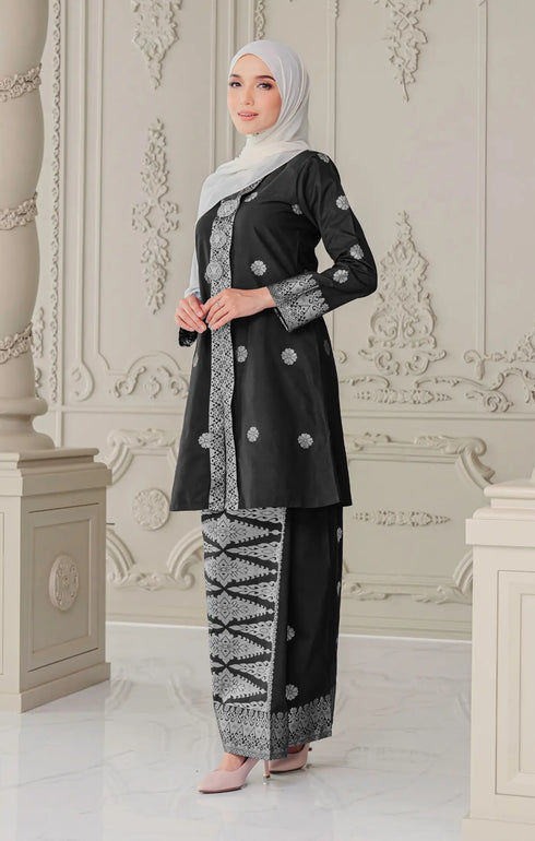 Woman wearing a Kebaya Black Silver showing premium songket texture and shawl white traditional outfit in an ornate room.