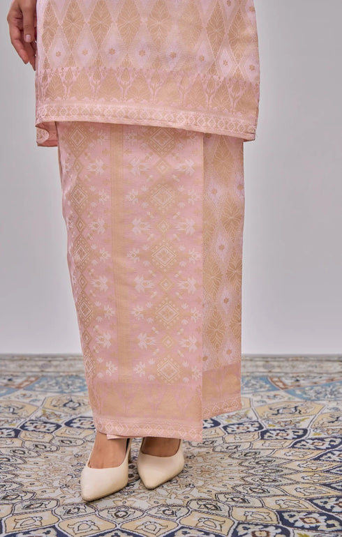 Model showing a Kurung Moden Baby Pink Gold traditional outfit with a brocade design on a patterned floor