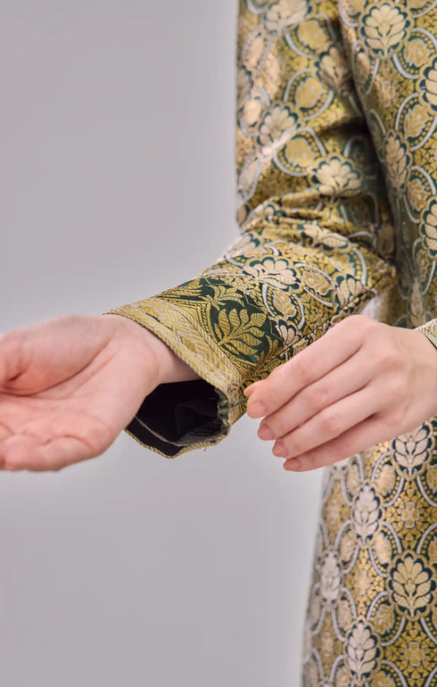 Fabric close up Kurung Moden Emerald Green Gold showing dyed brocade texture on plain background
