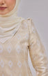 Woman wear Kurung Moden Off White Gold showing dyed brocade texture with a matching shawl hijab on a plain background