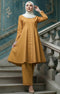 Woman in Kebarung Klasik Plain Mustard outfit standing on a staircase with decorative walls.