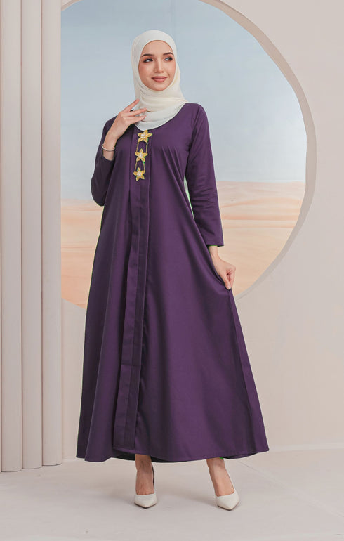 A model wearing a Jubah Kebarung Klasik Dark Purple, V-neck, long-sleeved, cotton plain traditional dress with a side pocket, standing in a circular mirrored background.