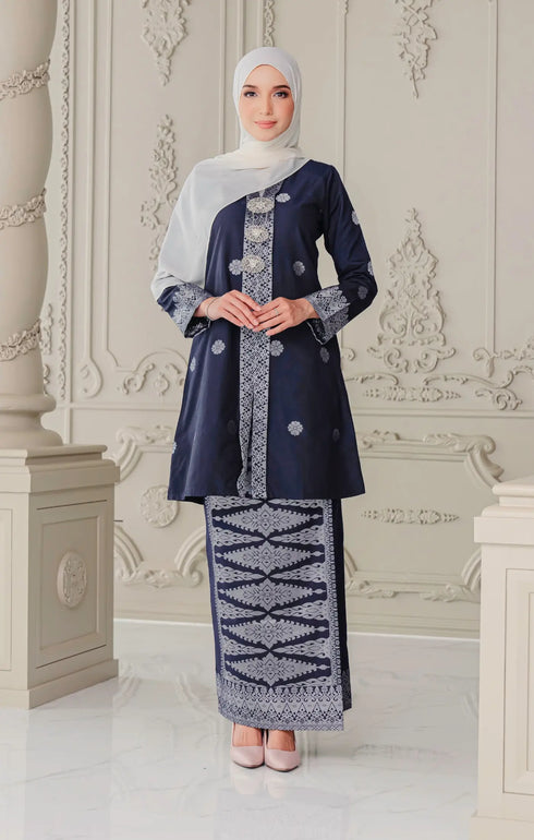 Model wearing Kebaya Blue Black Silver traditional outfit displaying overall styling and drape with shawl white hijab in an elegant interior setting