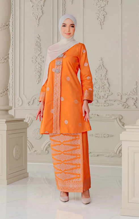 Woman wearing a traditional outfit Kebaya Orange Silver highlighting long sleeve and slim with a Instant Shwal white hijab in a decorated room.
