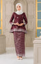 Woman wearing a traditional Kurung Kedah Dark Maroon Silver and white outfit with a matching shawl hijab in an elegant interior setting.