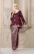 Woman wearing a traditional Kurung Kedah Dark Maroon Silver and white outfit with a instant tudung hijab against an ornate wall.