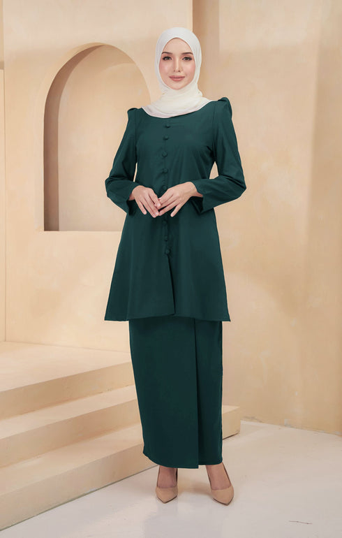 A woman wearing a Kurung Riau Plain Dark Emerald Green kurung with a round V-neck cut, long straight sleeves, and a back zip.