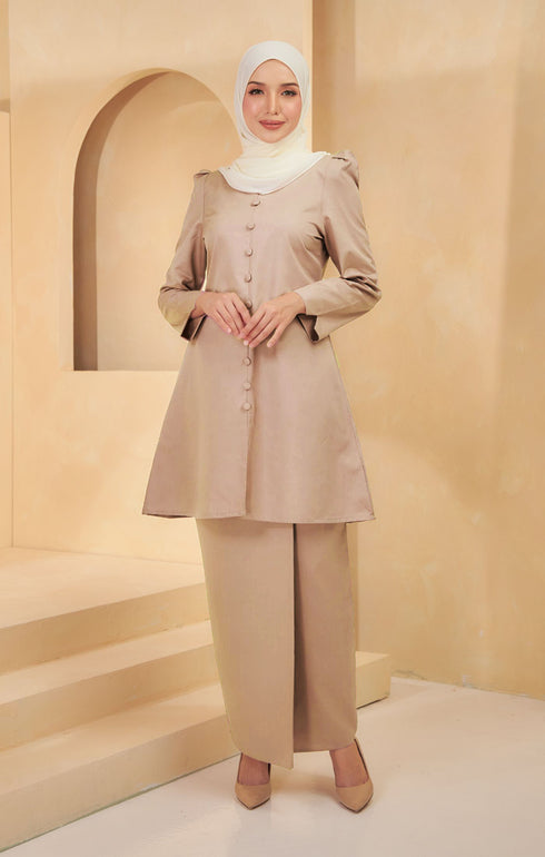 A woman wearing a Kurung Riau Plain Light Coffee, slim-fit traditional with long straight sleeves and a round V-neck cut, paired with matching trousers.