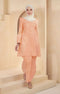 A woman wearing a Kurung Riau Plain peach-colored traditional outfit with a V-neck top and long straight sleeves, standing in a modern setting.