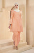 A woman wearing a Kurung Riau Plain peach-colored traditional outfit with a V-neck top and long straight sleeves, standing in a modern setting.