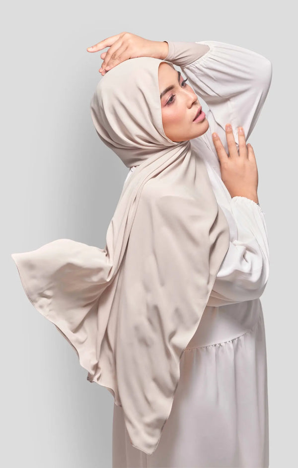 Woman wearing a Royal Satin Shawl Plain Hijab Sand front drape view showing full length and smooth satin fabric with White outfit against a light gray background