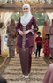 Woman in songket Bunga tabur burgundy traditional attires tanding on a decorated pathway with people in the background