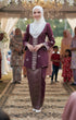 Woman in songket Bunga tabur burgundy traditional attires tanding on a decorated pathway with people in the background