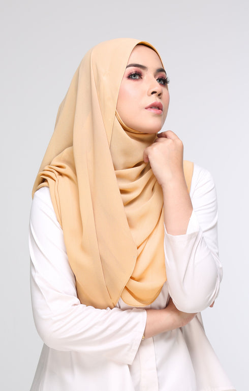 A woman wearing a Semi Instant Shawl Plain Nescafe Brown side view highlighting flowy edge and generous width around her shoulders, with a plain white top and blue eyeshadow.