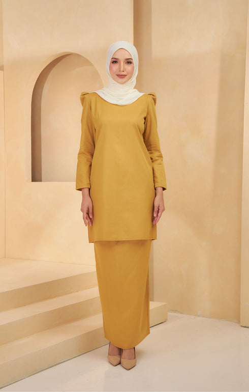 A woman wearing a Kurung Moden Plain Mustard front view traditional kurung set with a round neck and long sleeves, paired with matching trousers.