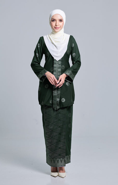 A woman wearing an Kebaya Dark Emerald Green Silver songket pattern, consisting of a long-sleeved top with a V-neck collar and a matching skirt, paired with a pearl white instanl shawl scarf